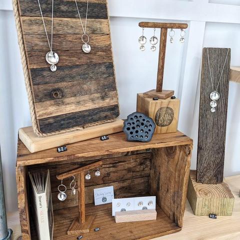 A selection of sterling silver necklaces and earrings, based on a domed and hammered silver disc, displayed on assorted wooden stands.