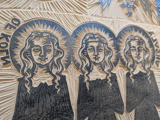 A linoleum block with a design representing the reliquaries of St. Ursula and her entourage in Cologne, Germany. It shows three stylized women with round faces and long wavy hair. The faces and hair are carved out but their bodies aren't yet.