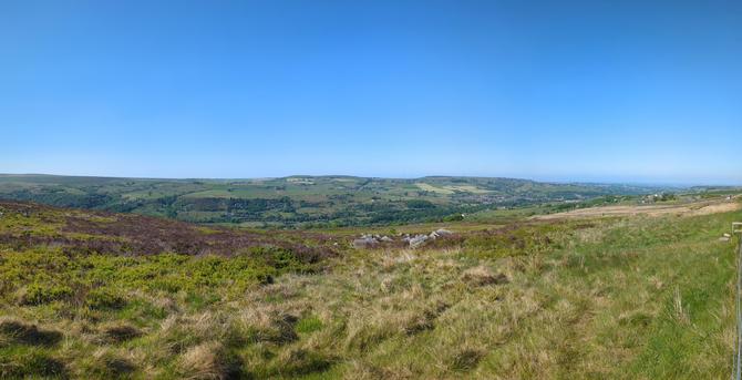 View down a moor side over a valley with fields and settlements stretching away lower down the valley towards the far distant horizon