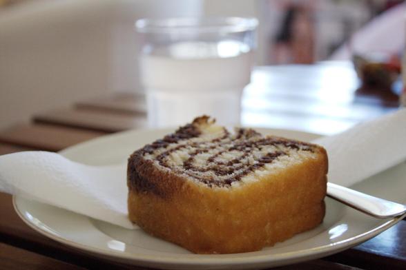 A table with a Swedish tiger sponge cake on a plate, and a glass of lemonade in the background.
