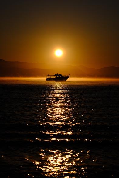 Sunrise over the Albanian Mountains from Corfu with a silhouette of a boat on the sea