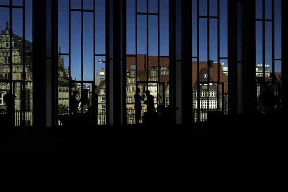 "Shooting Roland", Bremen — 13.05.2025 | 28mm • ƒ/8.0 • 1/400s • ISO 125

After shooting the Roland as a group exercise, our instructor managed to get us into the state parliament of Bremen which is right in front of the Roland. The Idea was to ask if we could shoot from the first floor windows, however we even got a private tour and where allowed into the other rooms aswell. 

While everyone else was shooting the Roland from the window of the ceremonial hall, I found it more interesting to shoot a panorama view of the giant glass facade, with focus on the bright outside view and all the class participants as black silhouettes in front of it. It took me a while to get the settings right, and unfortunately the best shot does not have every window occupied with one photographer (as it was the case in some of the pictures where the settings are unfortunately off), but I still like it :)