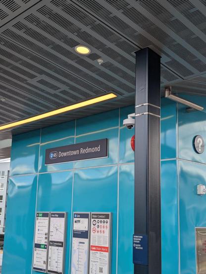The station at Downtown Redmond, with a light blue wall with maps and other normal station signage, with the station sign above it that says 2 (station number 65), Downtown Redmond
