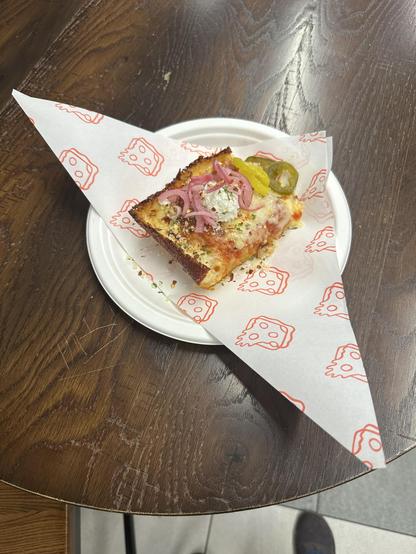 Photo of Detroit style pizza on a plate. The wrapper is folded in a triangle shape that resembles wings.