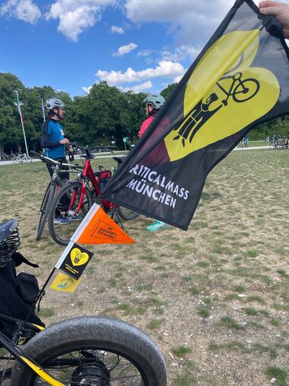 Ein „Fahnenmast“ an einem Rad mit den Wimpeln des Radentscheid Münchens, des ADFC, der CM München und einer großen Fahne der CM