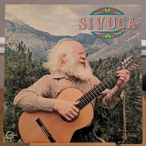 front cover with photo of Sivuca, with long white hair & beard, strumming an acoustic guitar outside in the mountains, eyes closed and smiling