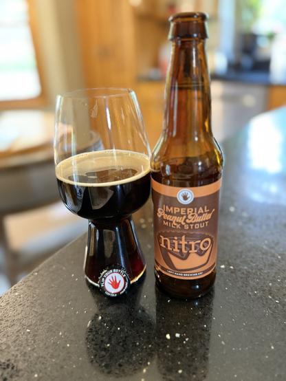 A stout glass of dark beer with the bottle cap in front. The red LeftHand logo is there. The brown bottle has a brown and orange label.