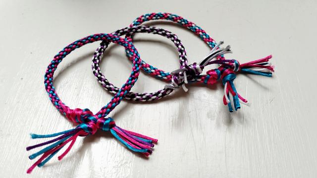Three kumihimo bracelets in various pride flag patterns (bi, ace, trans).
