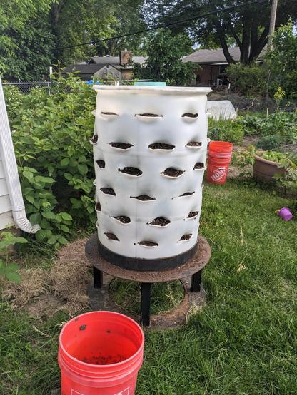 a big white plastic barrel on a stand with holes cut and bent in the sides to allow plants