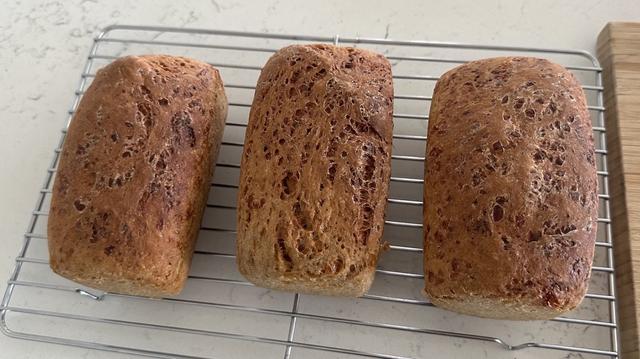 Three loaves of bread sitting on a cooling rack