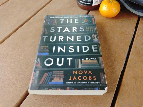 "The Stars Turned Inside Out" by Nova Jacobs on a table, with a tangerine I'm about to much.