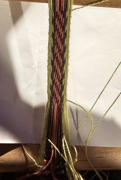 a thin band being woven. the exterior is light and dark green, while the centre part is a mix of red and pink that resembles a barbershop sign.