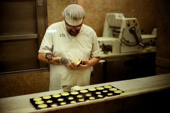 Colored photography of a tattooed cook preparing pastries (pasteis de nata).