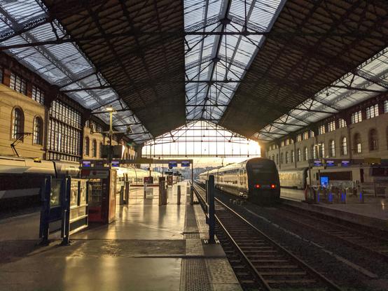 Une gare au petit matin. Sous un toit partiellement couvert par une verrière, et une charpente métallique légère mais aux dimensions magistrales, des quais s'élancent vers la lumière. Plusieurs train attendent leur départ, forcément imminent.