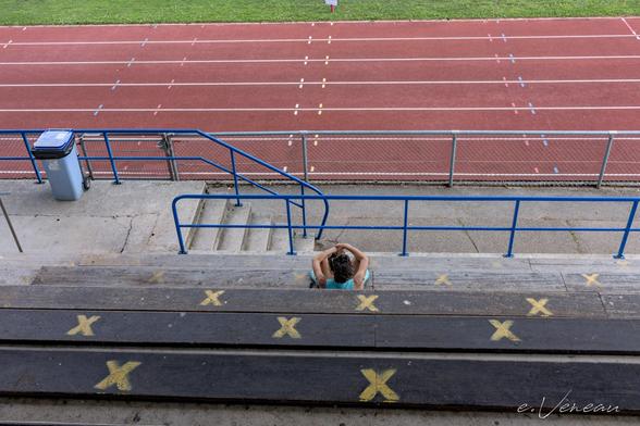 Stadium bleachers and running tracks seen from above. On the benches, crosses in yellow paint and a woman dressed in blue.