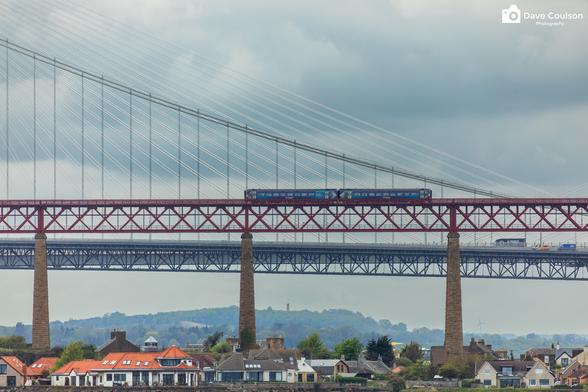 A photograph of the end of the Forth Bridge in North Queensferry with a small local ScotRail train moving across the bridge.