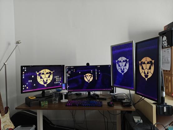 Monitore mit violett-goldenen Wallpaper; einer im Landscape-Modus links, einer im Landscape-Modus vorne / mitte, und zwei hochkant / portrait mode rechts
