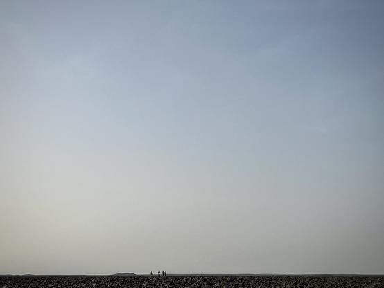 A landscape view looking at the horizon with some tiny human figures visible as silhouettes in the distance.