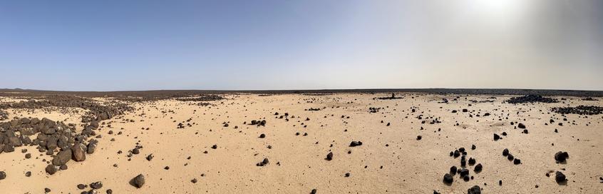 A panoramic shot showing a sandy desert and black basalt view.