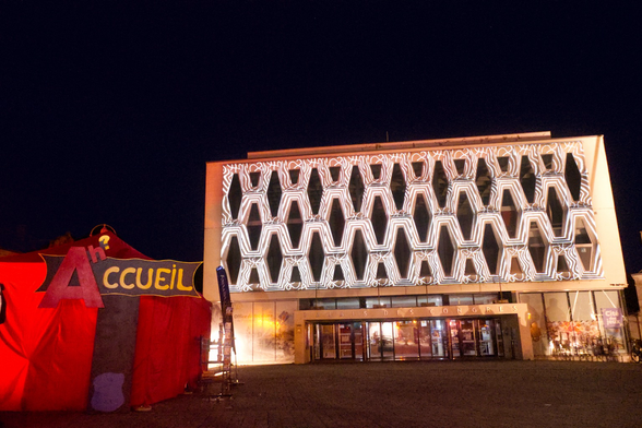 Projection d’illustrations sur un bâtiment année 80 devant une tente rouge