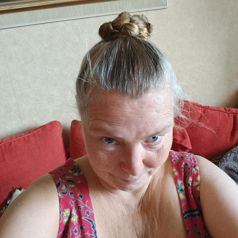 The head of a white middle aged woman in a dark pink dress, with a tight, braided bun of hair