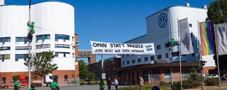 Robin Wood Aktive befestigen ein Banner am Eingang eines VW-Werks. Darauf steht:


ÖPNV STATT PANZER
JOBS NICHT AUF KRIEG AUFBAUEN