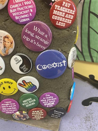 Another button says, "Coexist". The letters of the word include a Crescent Moon, a Peace Sign, a Star of David, and a Cross.