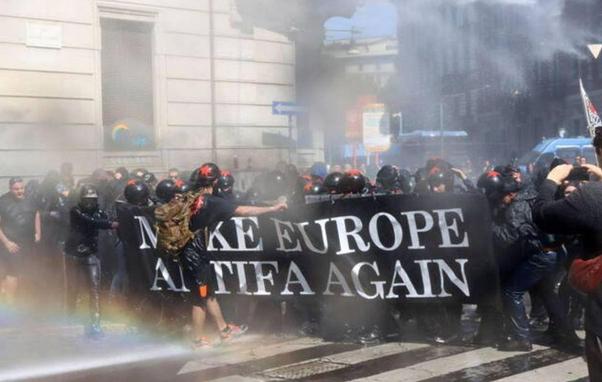 Ein vom Wasserwerfer nassgespritzter schwarzer Block mit dem Transpi "Make Europa Antifa Again"