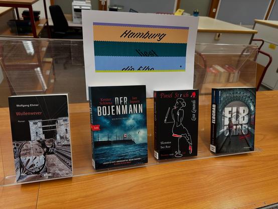 Eine Ausstellung in einer Bibliothek mit vier Büchern: "Wullenwever" von Wolfgang Ehmer, "Der Bojenmann" von Kester Schlenz und Jan Jepsen, und "Pinsels Strich" von Lisa Lemnitz