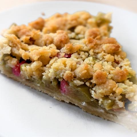 Ein Stück Rhabarberkuchen mit knusprigen Streuseln auf einem weißen Teller. Die grün-roten Rhabarberstücke sind im Anschnitt gut zu erkennen.
Foto by Johann Seidl, Gartenpoet.