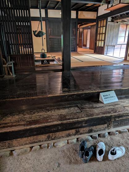 Inside of an old (around 1700s) farmhouse of a village administrator. It shows three different types of floor: in the foreground, stone floor for dirty shoes and messy work; then wood steps and walking area for high traffic zones; then tatami mats around an inset fire pit for sitting and relaxing. The fire pit has an iron kettle and a fish shaped pot hook hanging above it.