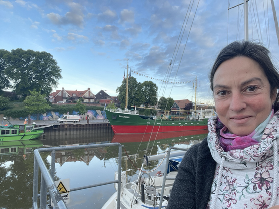 Frau steht vor Hafenbecken von Stade, altes Museumsschiff im Wasser. Dahinter alter Stadtkern mit großen Bäumen