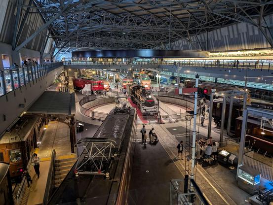 A photo of a huge indoor space scattered with many different train cars and engines, shot down from a second floor balcony.