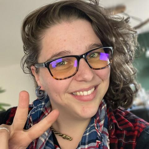 White author with glasses, smiling at the camera and doing a peace sign with two fingers of her right hand.