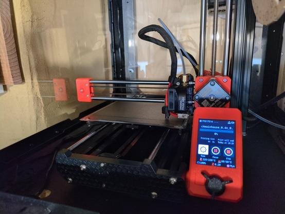 Photo showing Prusa mini 3d printer printing with black pla material inside a prusa housing.