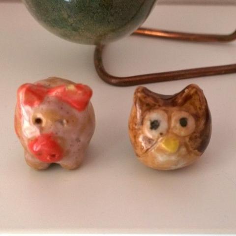 "These are two small animal figurines, one shaped like a pig and the other like an owl, placed on a surface. The pig has a pink nose."