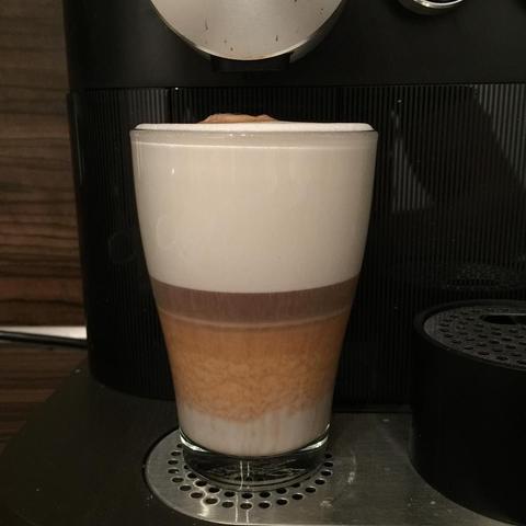 This picture shows a latte art cappuccino being prepared in an espresso machine. The latte art has two distinct layers resembling a heart shape, indicating a high level of skill and precision in the brewing process. The foam on top is fluffy and well-textured.