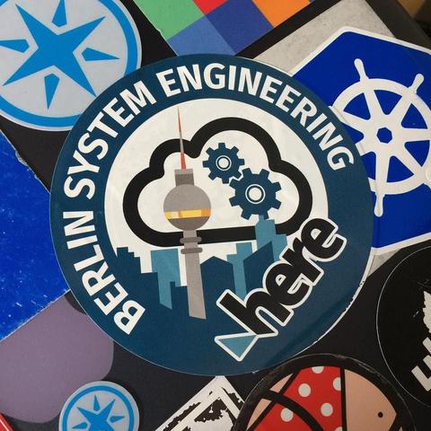 "This picture shows a sticker on a laptop. The sticker features a cloud-like graphic with the words 'Engineering' written within it, along with the name 'Berlin System Engineering'. There is also a depiction of a ship or boat icon above this text. Below the cloud image is the word 'Here', suggesting that it might be an advertisement or a sign indicating the presence of such services in the location shown. The mood of the picture appears to be promotional, possibly aimed at tech-savvy individuals interested in Berlin System Engineering."