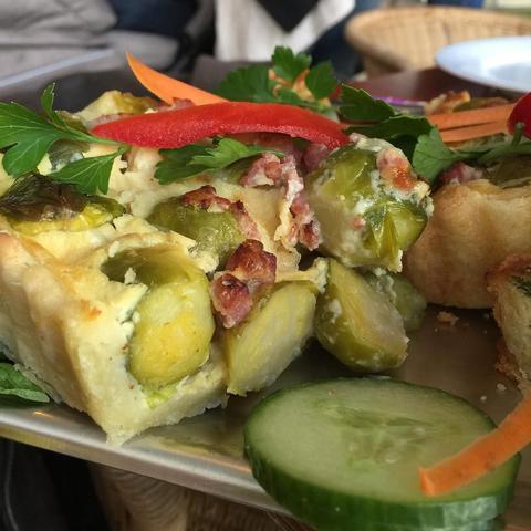 "This picture shows a plate of food including a piece of breaded with feta cheese and vegetables, served on a metal tray atop a wooden table. The food has an appetizing appearance and the overall mood is inviting and enjoyable."
