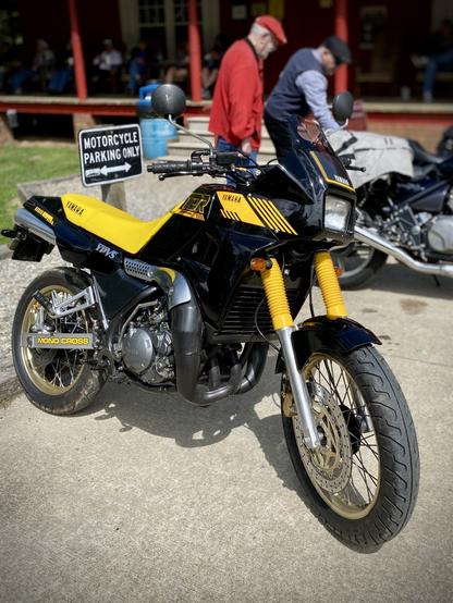 A vintage Yamaha TDR 250 motorcycle in beautiful condition parked in front of a sign that reads "MOTORCYCLE PARKING ONLY"