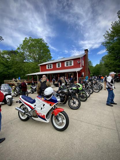 A row of motorcycles parked in front of a red lodge that looks like a red barn.  The sky is bright blue with whispy clouds and green trees in the background. 
The first bike in the row is a vintage Honda VFR750F Interceptor motorcycle.  Bayport's bike is in the middle of the row.