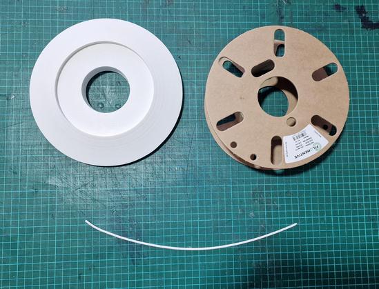 Green cutting mat with a white circular 3d model, and empty spool and a short curve of filament together making a smiley face.
