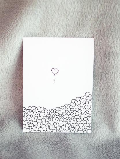 Eine Postkarte auf der mehrere Herzen zu sehen sind, während eines wie ein Luftballon hoch steigt 
s/w


A postcard on which several hearts can be seen while one rises like a balloon 
b/w