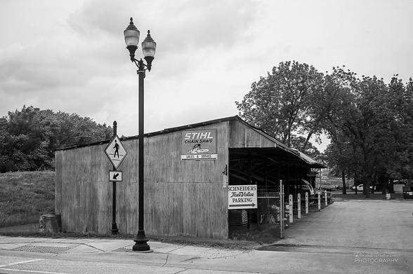 Black and white image of a three sided lumber and equipment shed at a small True Value hardware store.