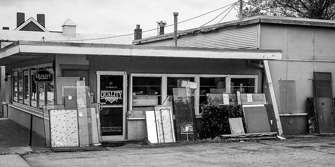 A black and white view of the side of a glass and mirror shop housed in a small one-story building.