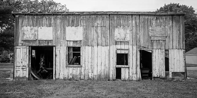 A large wooden shed/garage with peeling and weathered paint, broken windows, and a missing door.