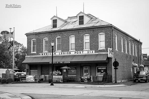 Exterior view of a two story brick building.  There are 6 tall windows on the front and side of the second story.  A sign over the awning says, "American Legion Post 313".  On the awning it says "Hobo's at the Legion" to identify a restaurant run on the first floor of the building.