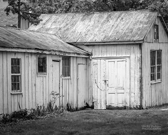 An old wood faced garage/shed with an old corrugated metal roof and weathered white paint.
