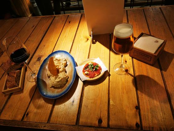 Tisch in einer Bar mit einem Bier, einem Glas Wein und 2 Tellern mit Pintxos. Ensaladina Rusa und Talochip den Atun rosa
