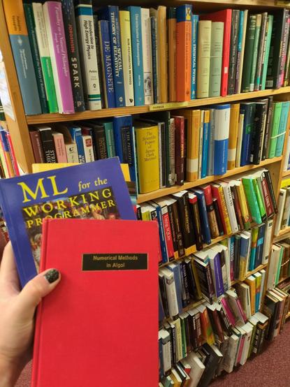 a densely packed shelf with books on computer science (operational semantics, patterns, simulation etc); in front of it i am holding two of my purchases, "ML for the working programmer" and "Numerical Methods in Algol"